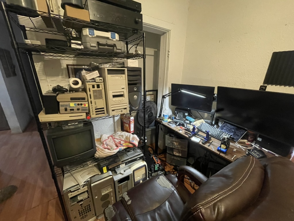 A Stack of Computers on a wire shelf next to a desk  covered in computer accessories